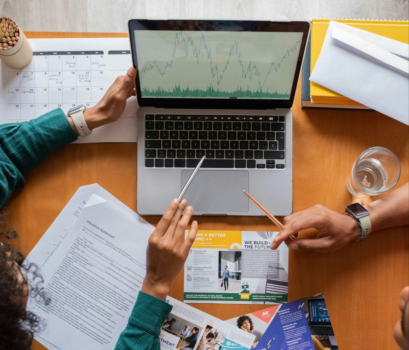 2 peoples hands pointing at a laptop with graph
