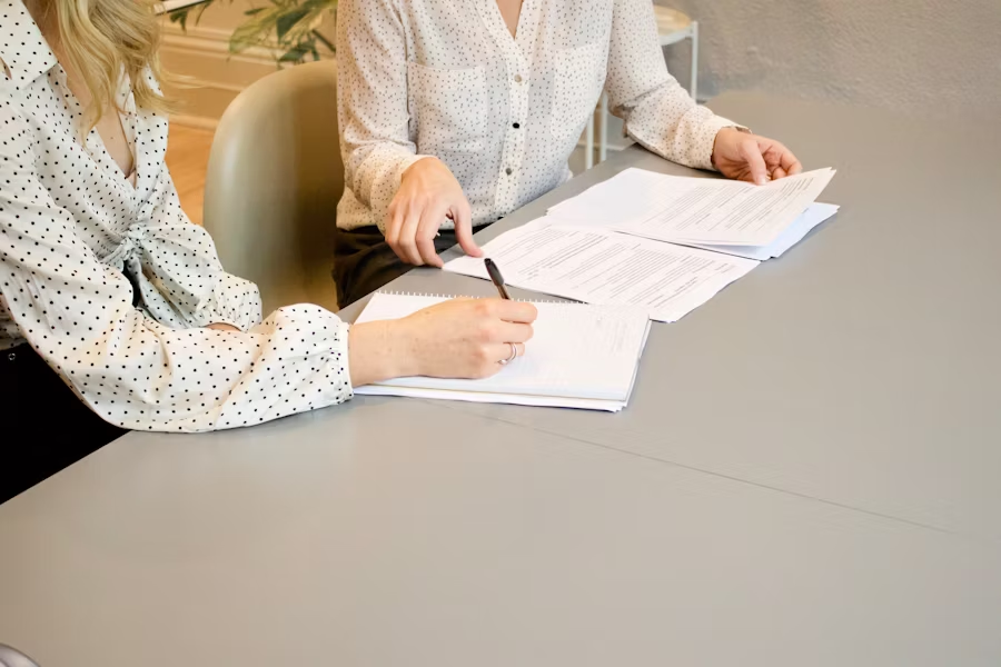 2 women sitting at a table signing paper