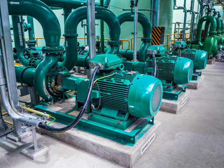 Row of green industrial pumps connected to large green pipes in a modern facility.