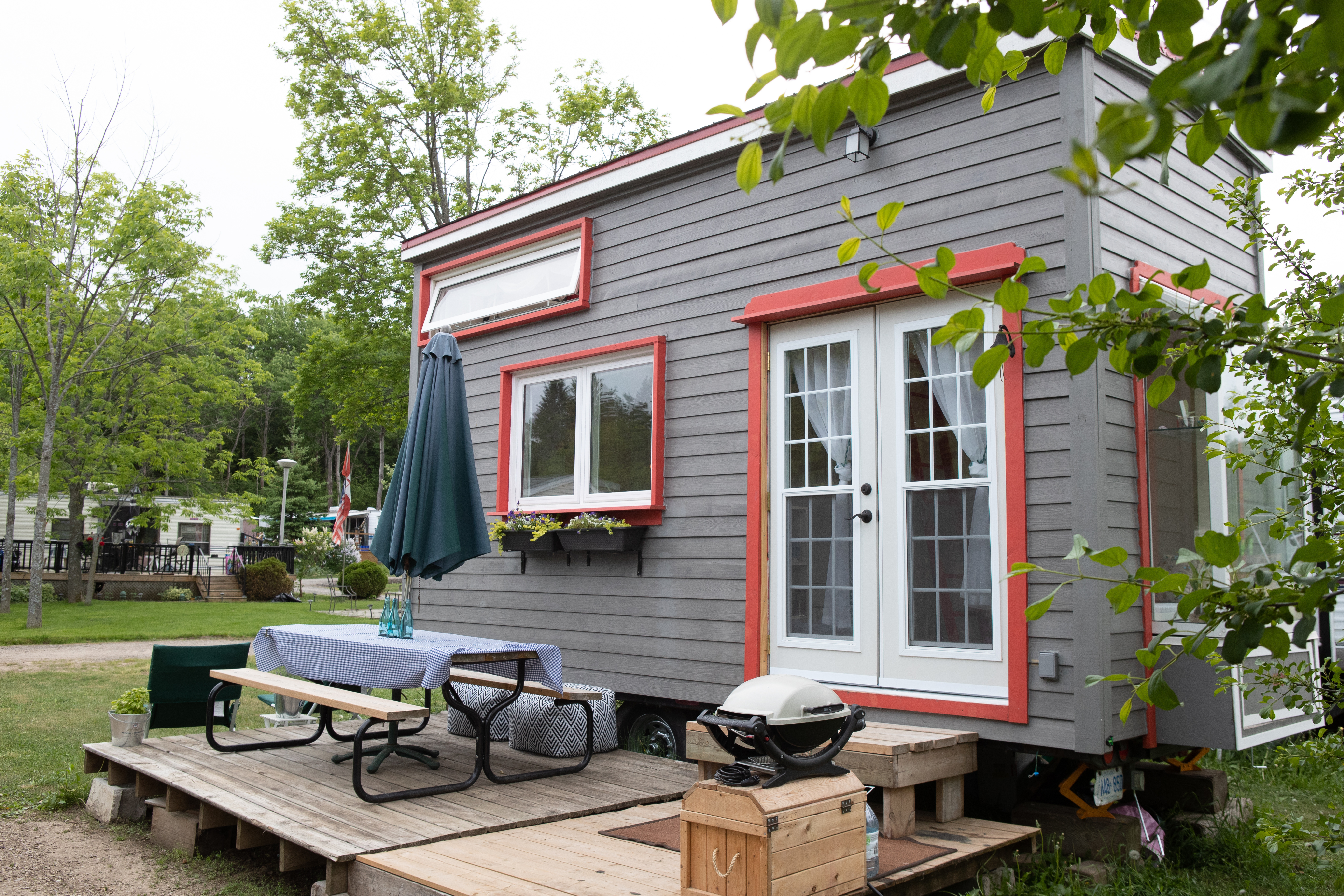 Tiny house with red trim and outdoor deck seating.