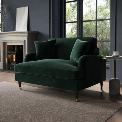 A luxurious dark green velvet loveseat with a fireplace and large window in a room with dark blue walls.