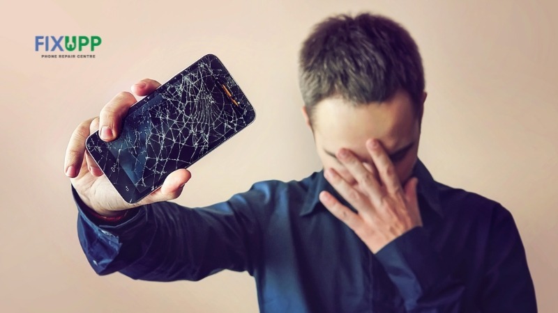 A man holding a phone with a broken phone screen