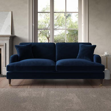 A modern navy blue velvet sofa with two pillows positioned in front of a large window.