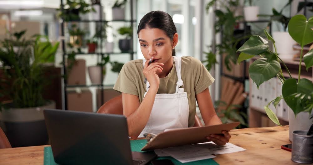 A small business owner holding a clipboard in front of her laptop -