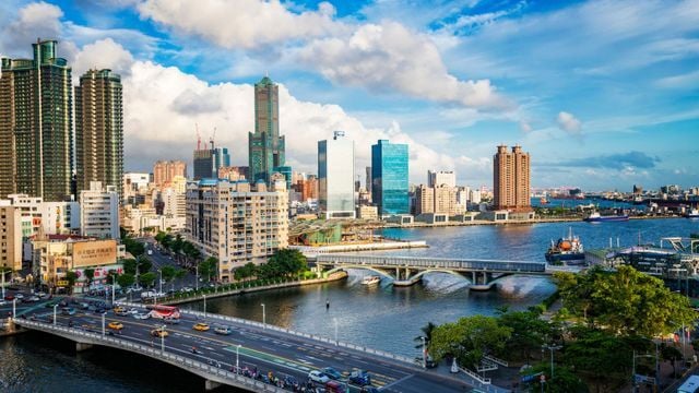 A vibrant cityscape featuring a large river crossed by multiple bridges, with a mix of modern high-rise buildings and older architecture under a partly cloudy blue sky.
