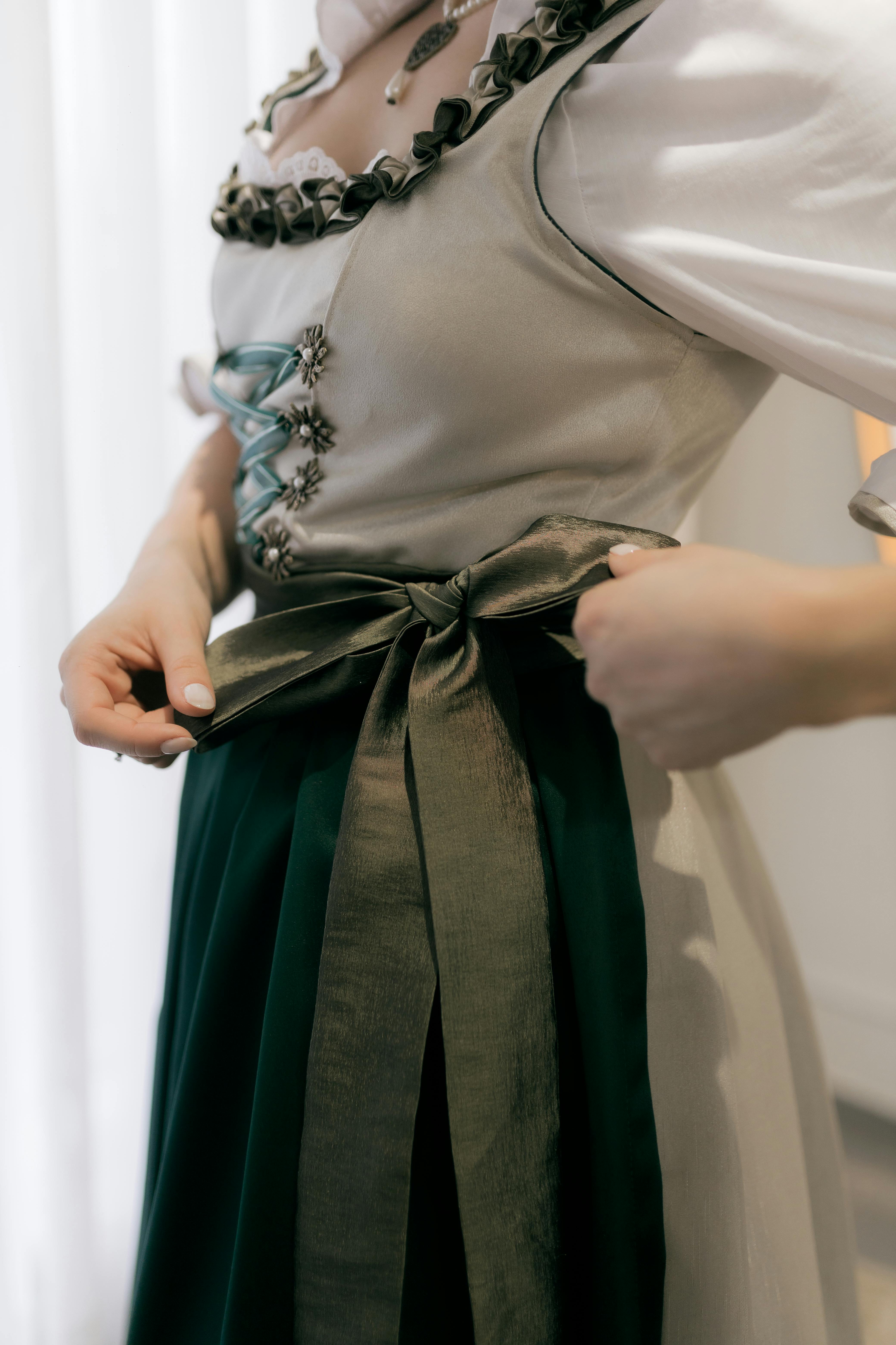A woman elegantly adjusts the bow of a traditional dress, showcasing its intricate design and craftsmanship.