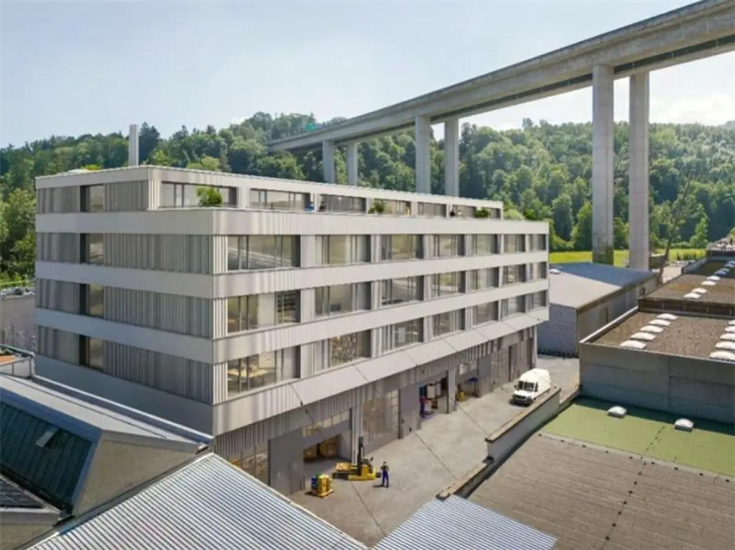 An industrial or commercial office building located next to a tall, concrete elevated bridge or viaduct, with a loading area featuring a white van and a forklift.