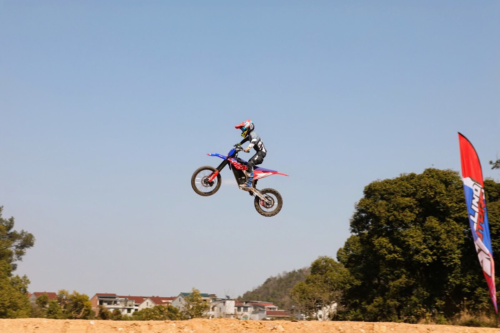 Rider mid-air on a red and blue RFN dirt bike during a jump.