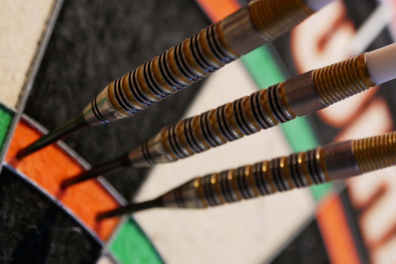 Close-up of three darts stuck in a dartboard, focused on the metal barrels and tips.