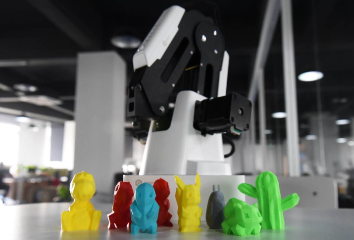 Several colorful 3D-printed figurines displayed in front of a 3D printer.