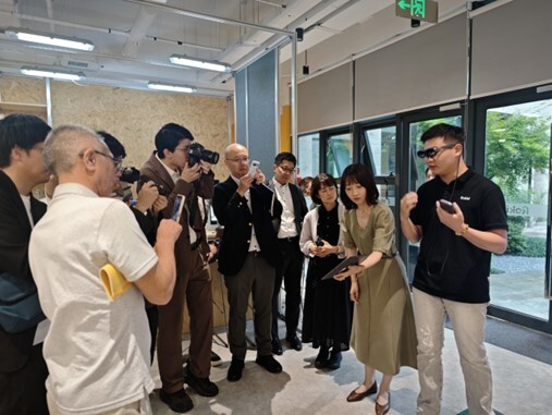 Group of people in a modern office space, some taking photos or videos, suggesting a presentation or event in progress.