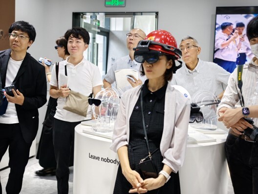 Group of people at an event, one wearing a red helmet, gathered around a table with transparent objects and a sign reading “Leave nobody.”