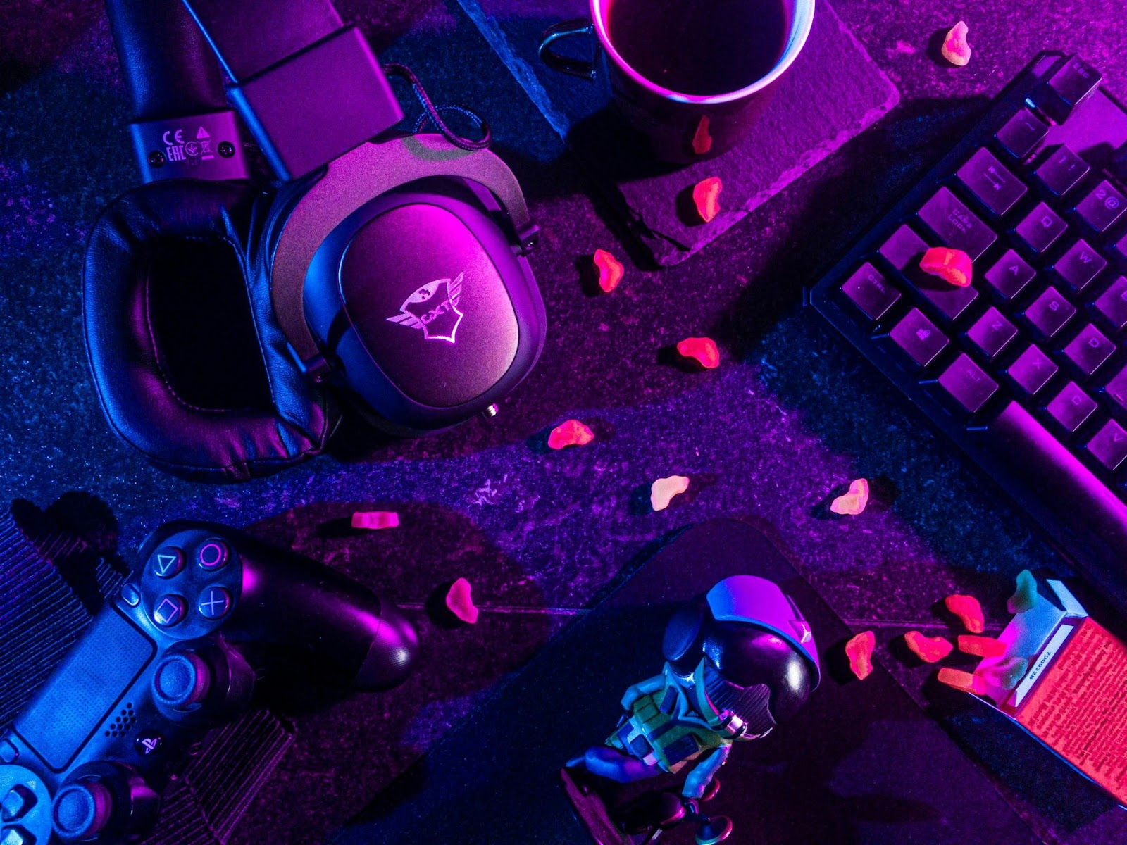 Gaming setup with headphones, controller, keyboard, and neon lighting.