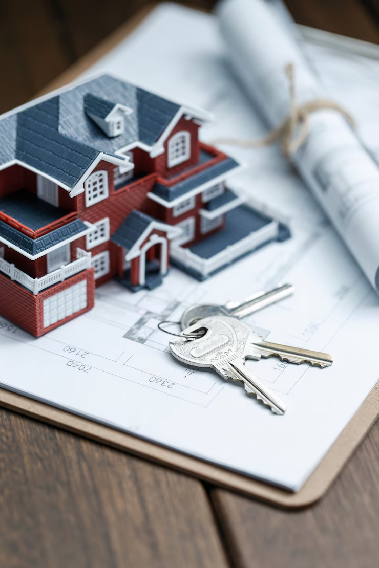 Miniature house, keys, and rolled-up blueprints on a floor plan drawing.