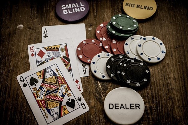 oker cards and chips, including "DEALER," "SMALL BLIND," and "BIG BLIND" markers, laid out on a wooden surface.