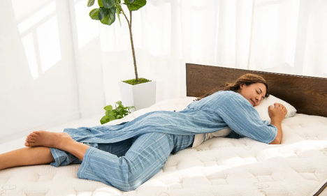 Photo of woman sleeping on her side on comfy mattress in a white bedroom with a plant nearby
