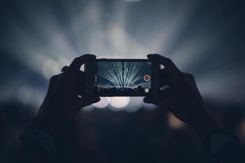 Pair of hands holding a smartphone recording a concert stage with bright spotlights.