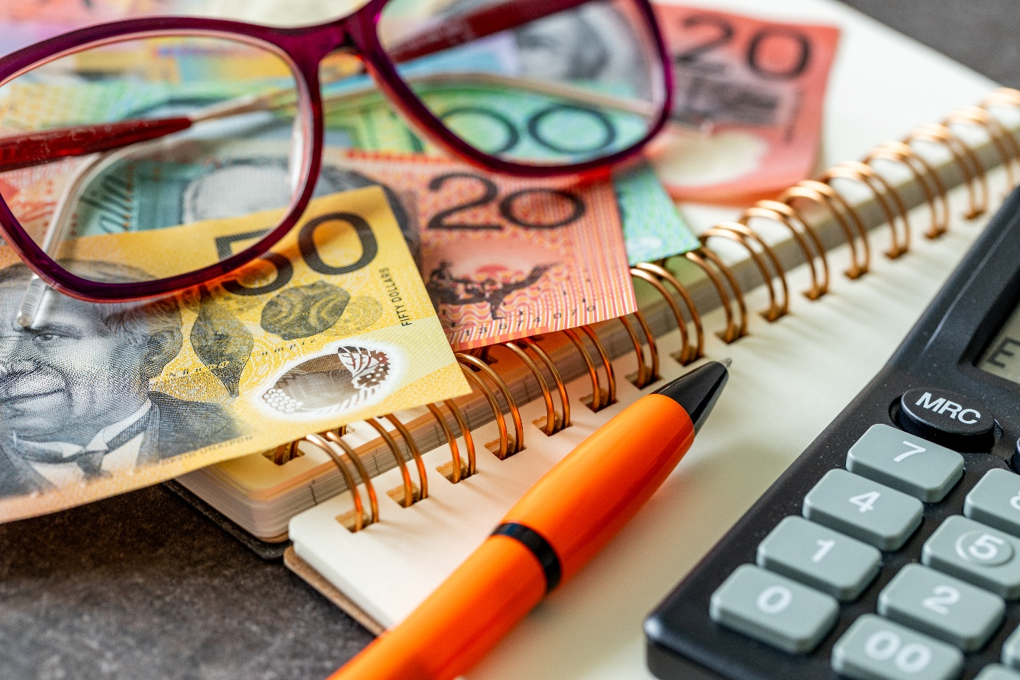 Picture of glasses, money, pen and calculator on a notebook