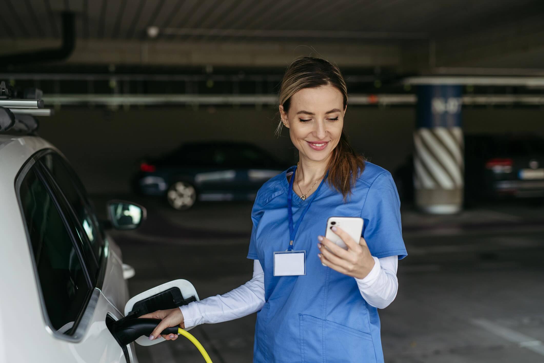 Woman in medical scrubs charging an electric car in a parking garage