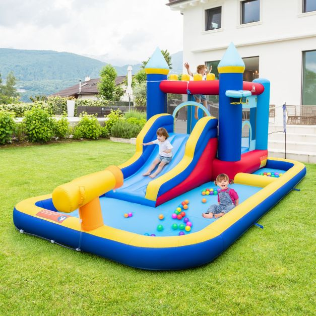 Two children playing on a large, colorful inflatable bouncy castle and water slide in a backyard.