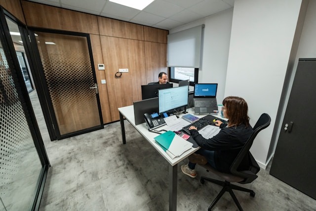 Two people working at their computers in a modern office with wooden walls and minimalist decor.