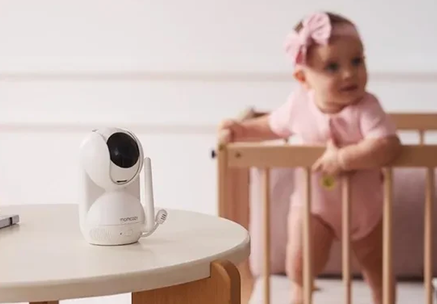 baby in a crib with a monitor camera on the table across the crib