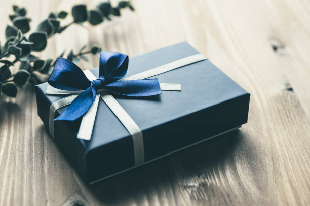 Why choose custom gift boxes - image of dark blue gift box with silver and blue ribbon on timber surface and sprig of leaves in background