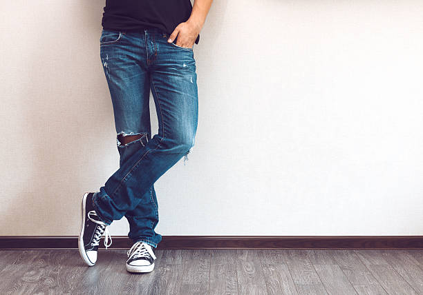 Photo of man standing against wall in size 15 sneakers navy and white with ripped jeans 