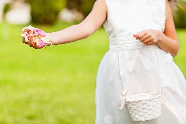Young girn in silk flower girl dress holding out handful of petals