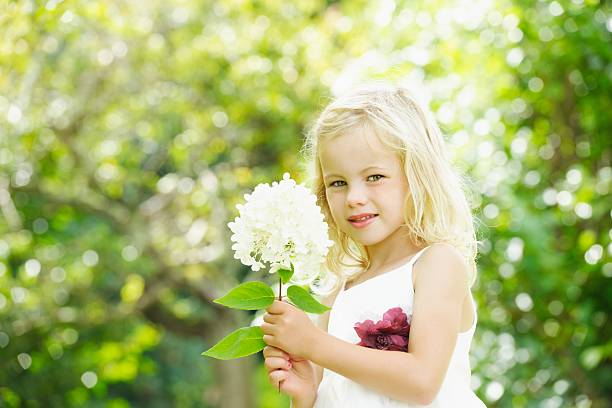 Young girl in silk flower girl dress holding flowers and looking to camera