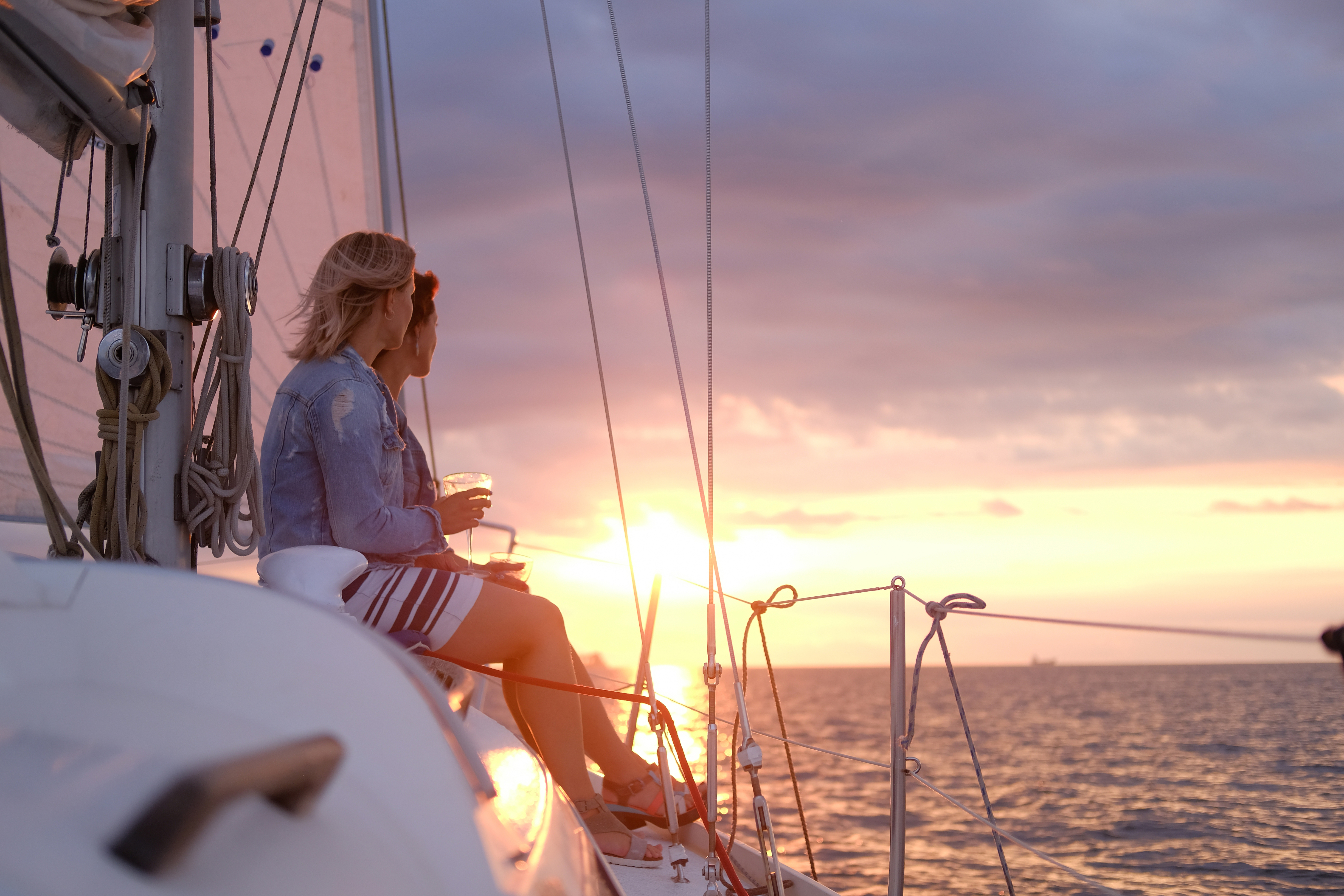 couple ladies are enjoying their trip sailing boat while drinking wine watching beautiful sunset