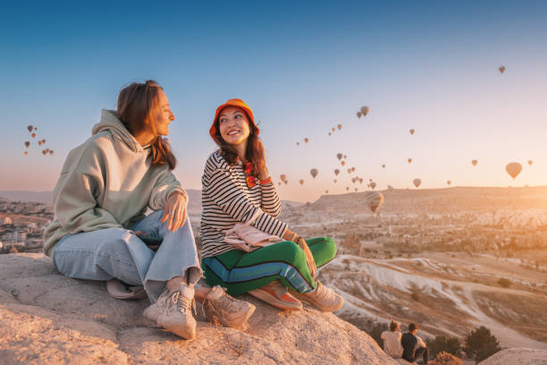 2 woman sitting at top of a big stone