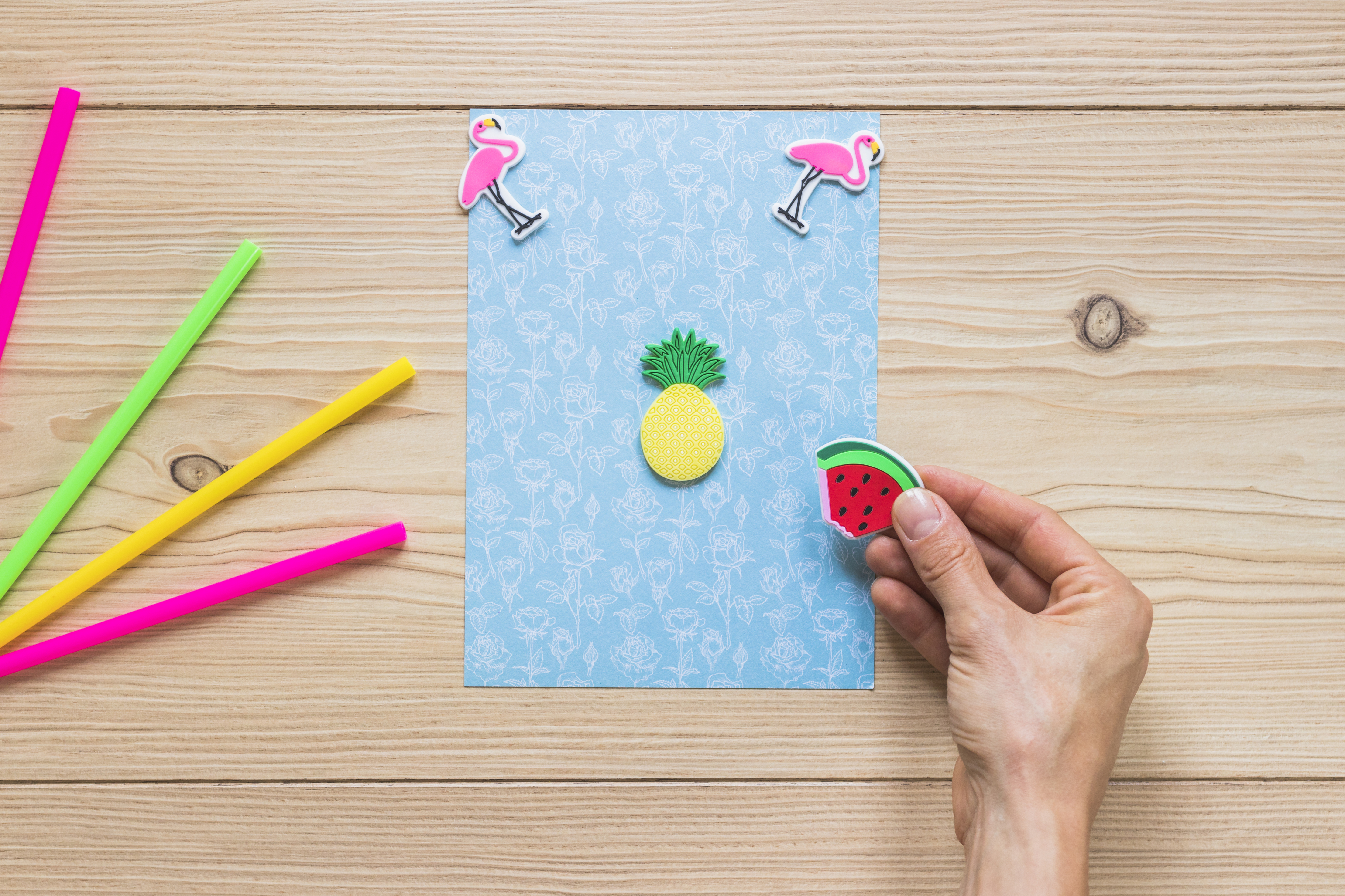 A person's hand decorating blue card with sticker on wooden background