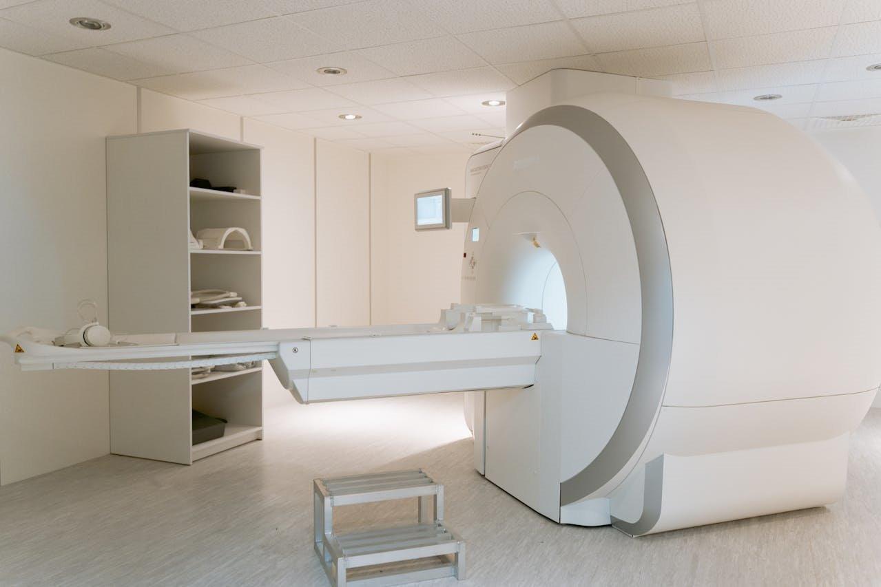 MRI machine in a clean, modern medical room with a patient table extended and shelves holding accessories nearby.