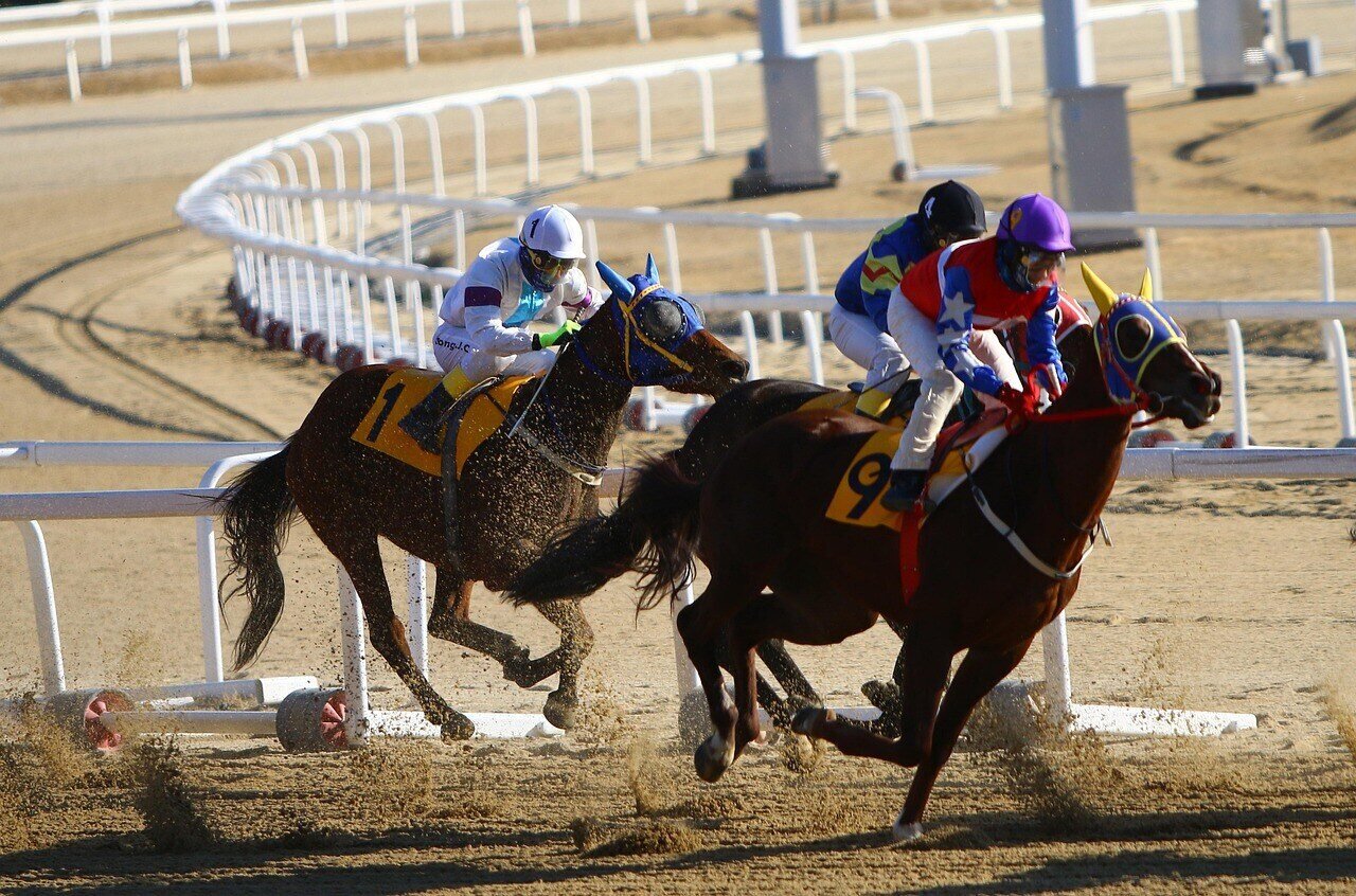 Three jockeys riding horses in a competitive horse race on a dirt track.