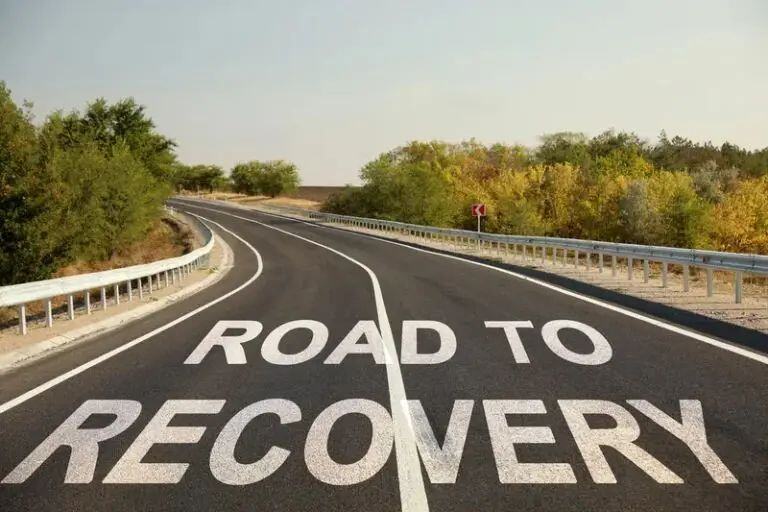 The role of sober houses in the road to recovery from addiction - a photograph of a curved road surrounded by trees with the words road to recovery imposed on the road in the style of white road lines