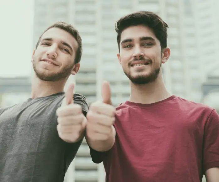 sober living houses - two men facing camera and holding their arms extended with their thumbs up