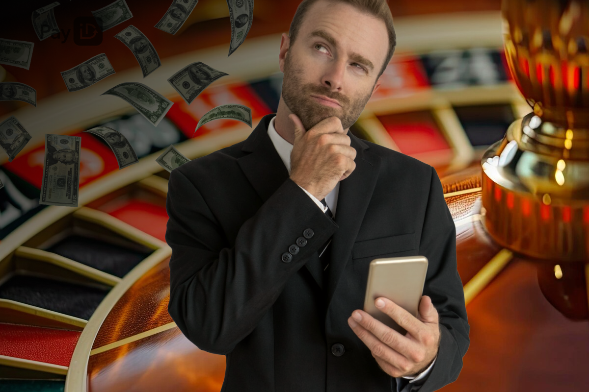 A man wearing a tux holding his phone in a blurred casino roulette table background while making a thinking face