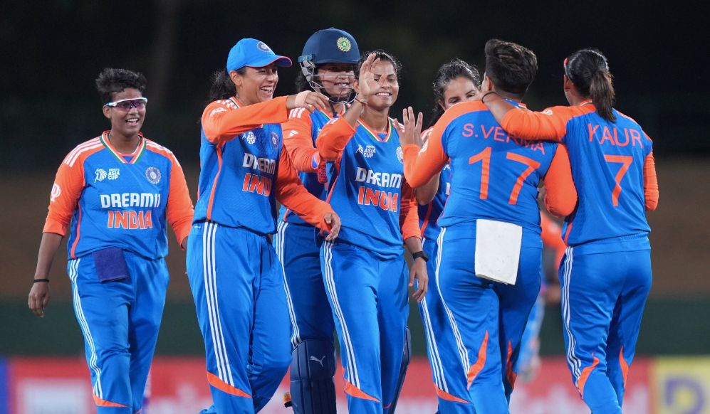 Indian women cricket players celebrating in a huddle, wearing blue and orange "DREAM11 INDIA" uniforms. "S. Verma 17" and "Kaur 7" visible.