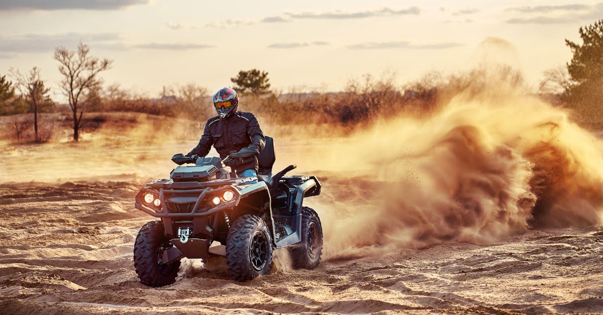 Person riding an ATV on sandy terrain, kicking up a large cloud of dust.